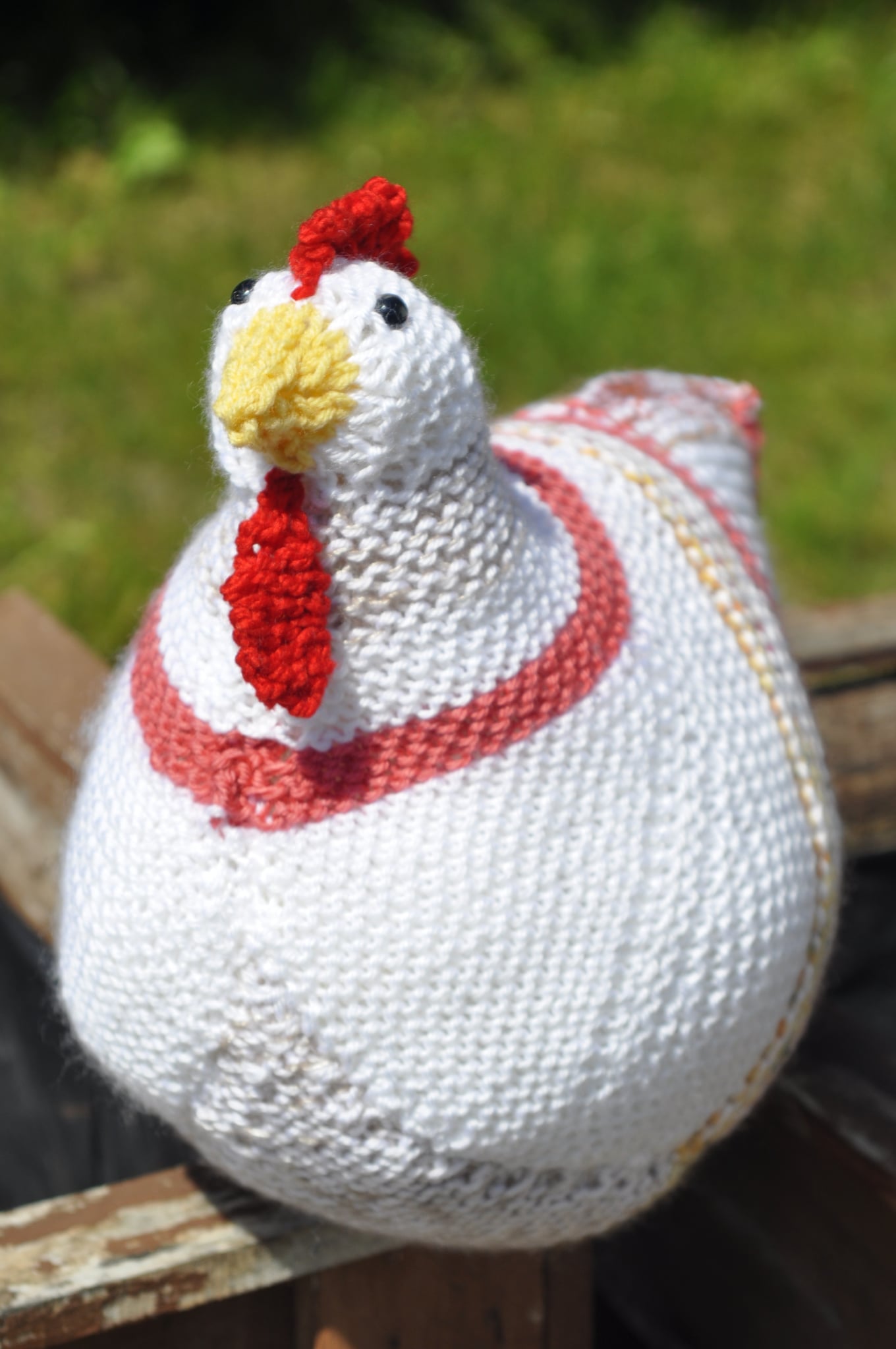 Poule tricotée blanche à motif rouge, perchée sur une clôture de bois